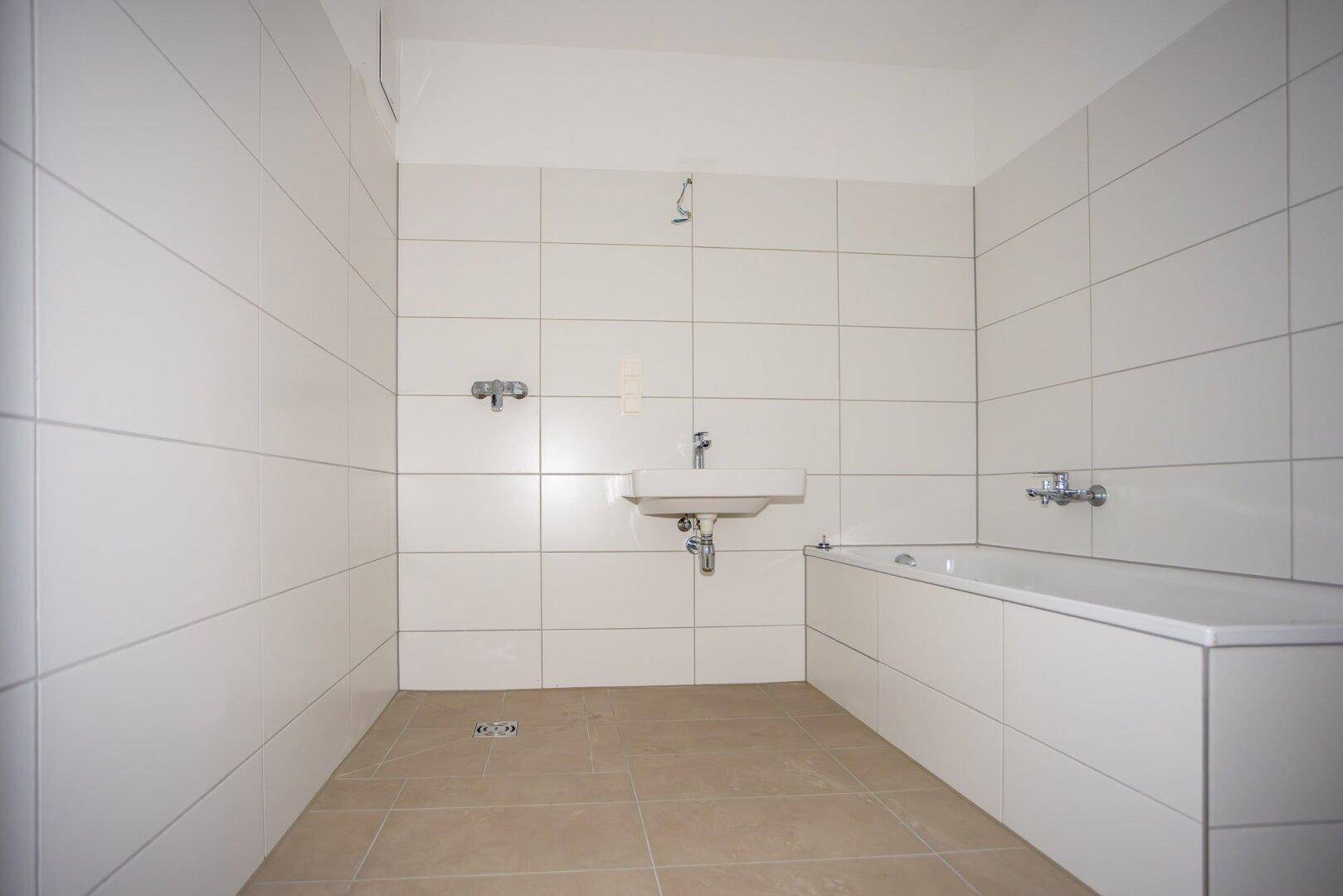 Modernes Badezimmer mit weißen Fliesen, Waschbecken und Badewanne, in neuwertigem Zustand.