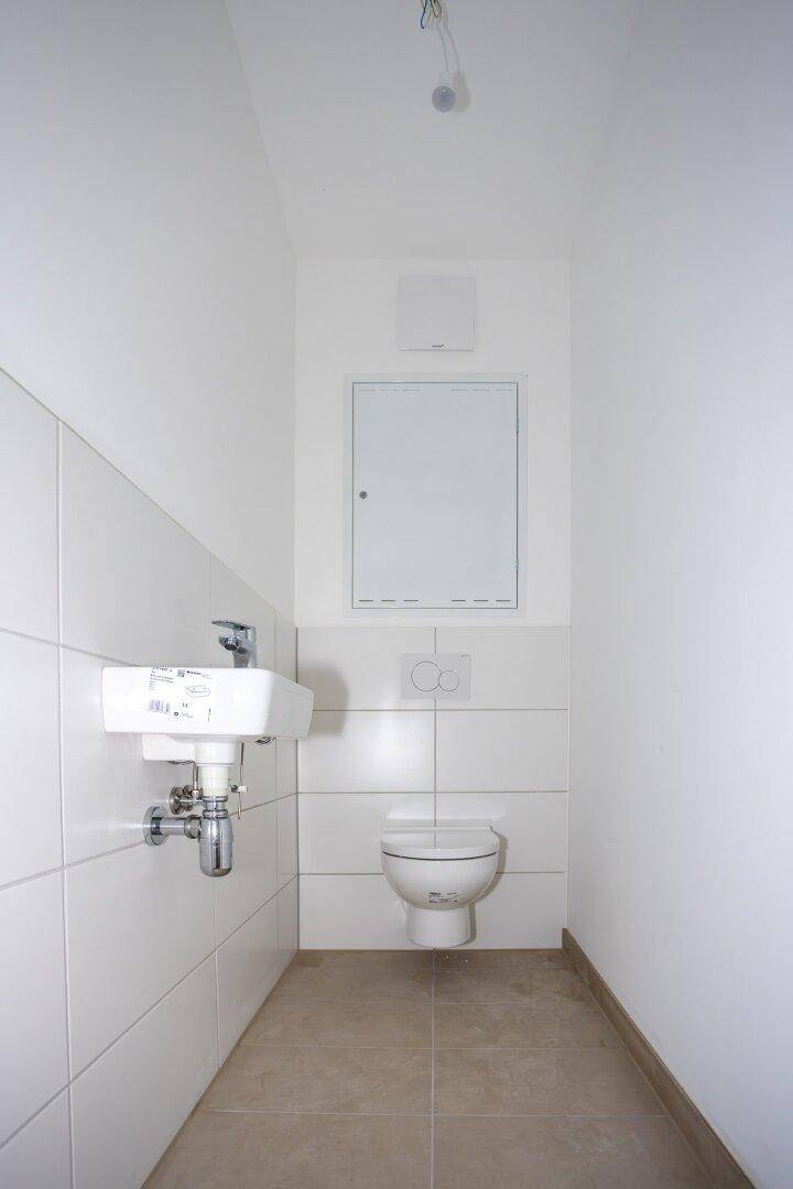 Kleines Gäste-WC mit Wand-WC, Waschbecken und weißen Fliesen, praktisch und modern.