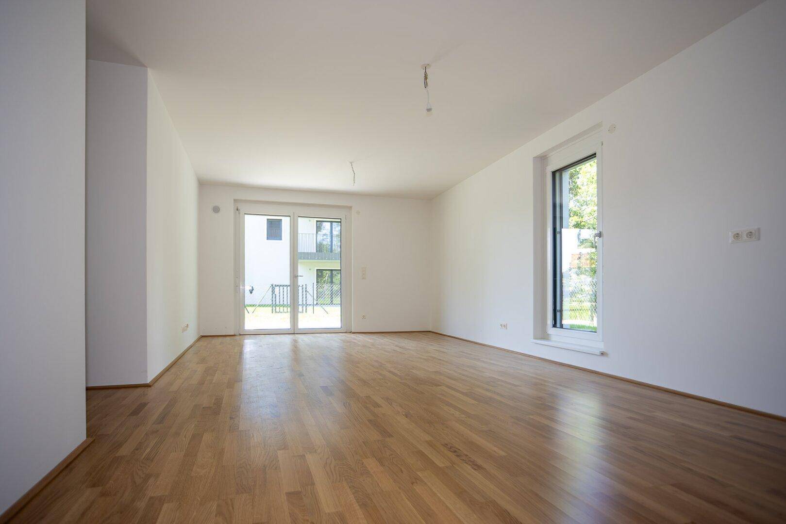 Geräumiges Wohnzimmer mit Holzboden, großen Fenstern und Zugang zur Terrasse oder Balkon.