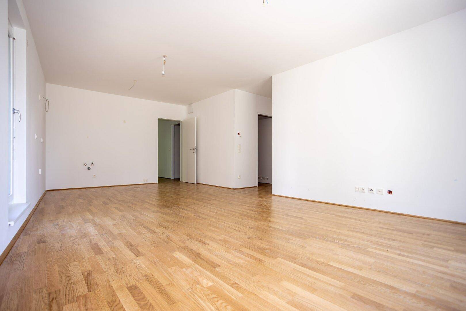Helles, leeres Wohnzimmer mit Parkettboden und weiß gestrichenen Wänden, bereit zur Einrichtung.