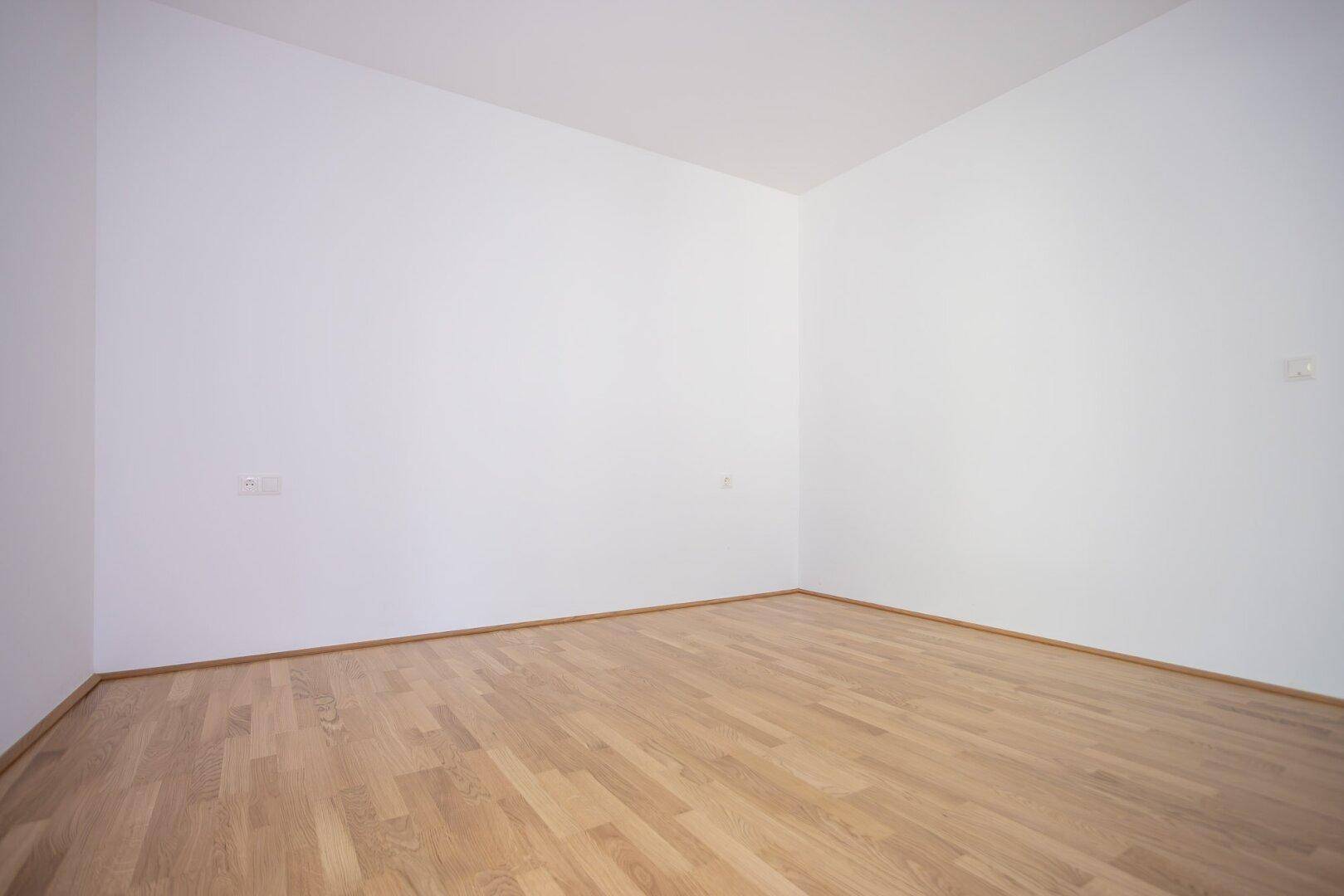 Leeres Zimmer mit hellem Parkettboden und weißen Wänden, bereit zur individuellen Gestaltung.