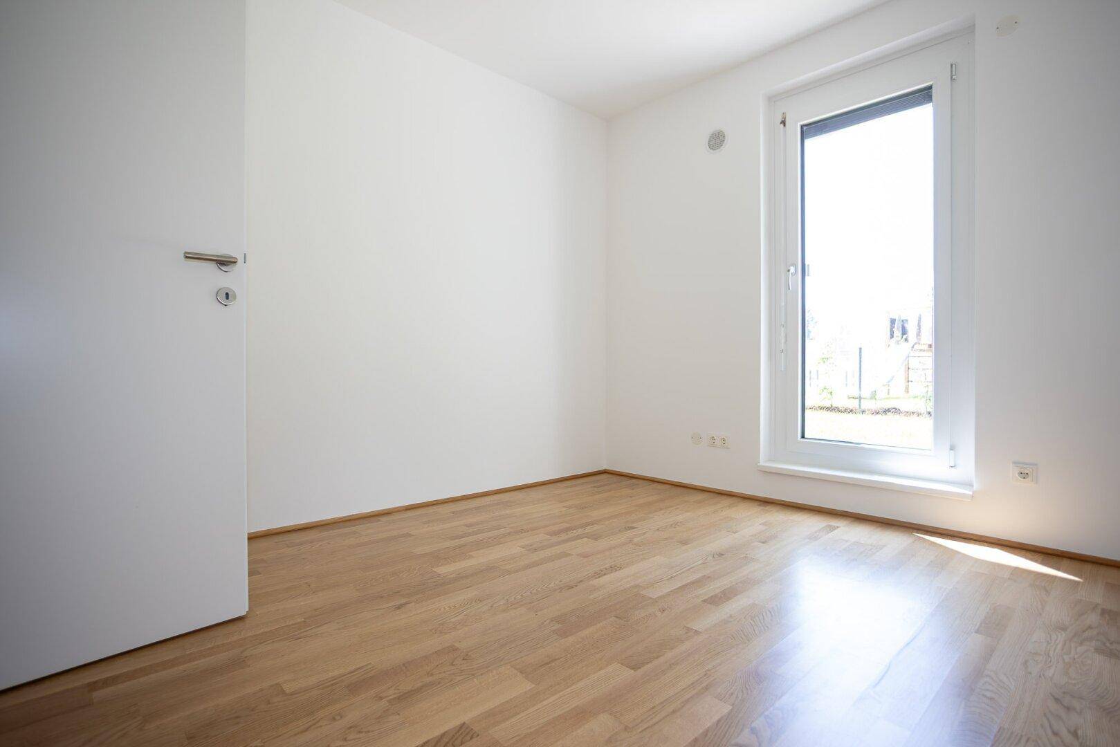 Helles Zimmer mit Parkettboden und großem Fenster, ideal für Schlaf- oder Arbeitsbereich.