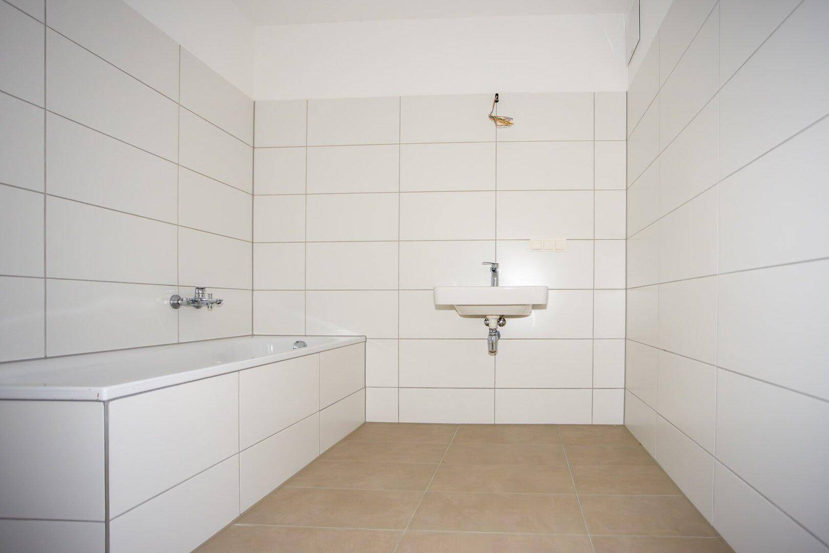Modernes Badezimmer mit Badewanne, Waschbecken und weißen Wandfliesen in schlichtem Design.