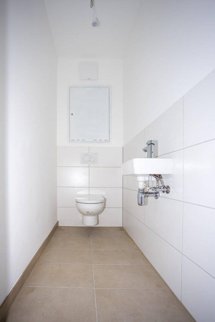 Kleines Gäste-WC mit Wand-WC, Waschbecken und weißen Fliesen in minimalistischem Stil.