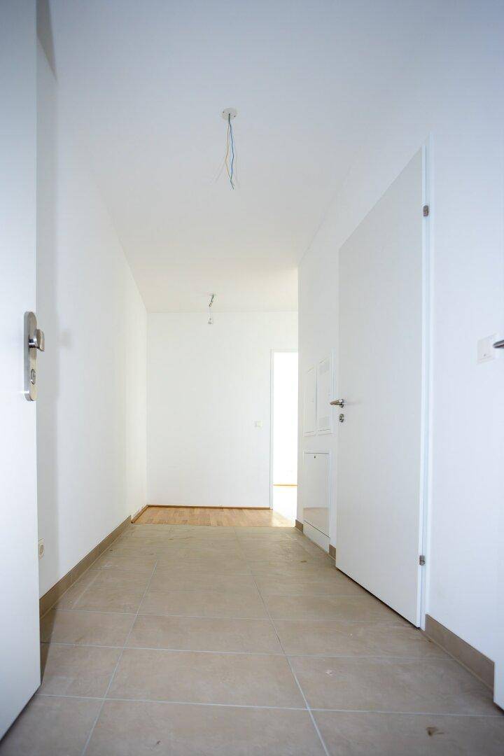 Heller Flur mit Fliesenboden und Zugang zu verschiedenen Räumen in einem Neubau.