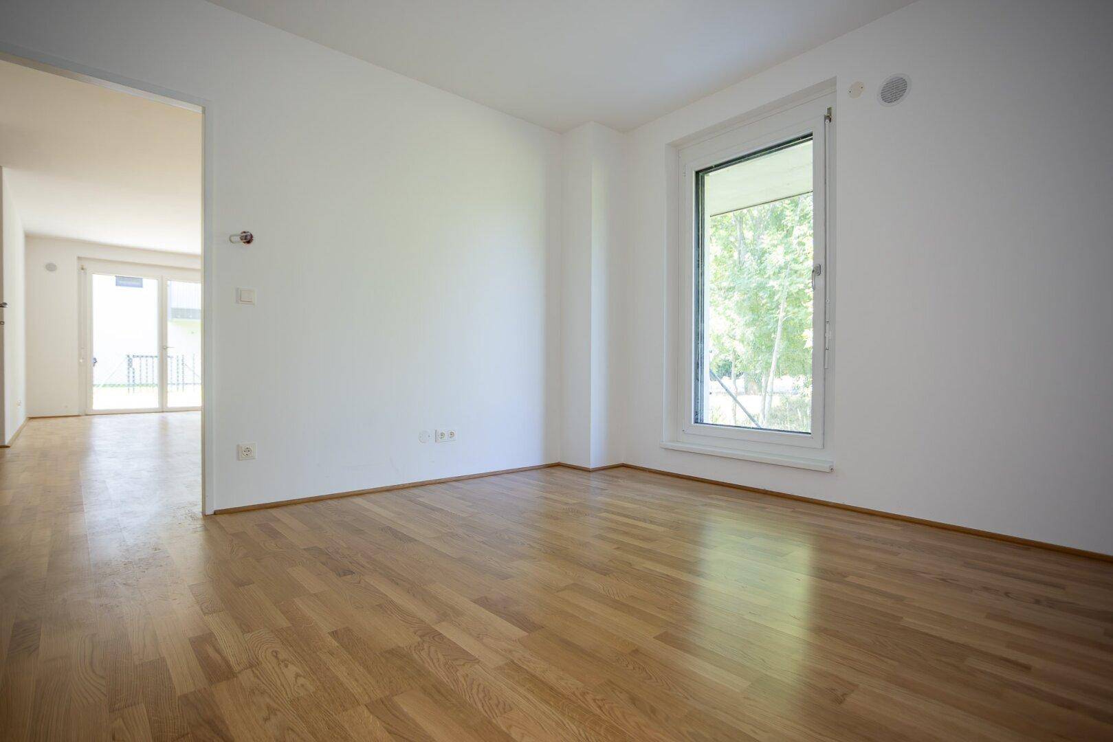 Helles Zimmer mit Parkettboden und großem Fenster, ideal als Schlaf- oder Arbeitszimmer.