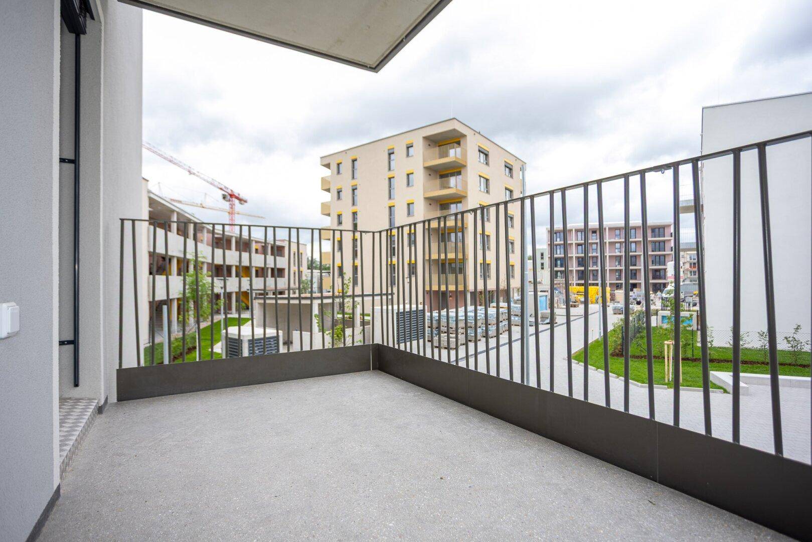 Balkon mit Blick auf eine Baustelle und weitere Gebäude unter einem bewölkten Himmel.