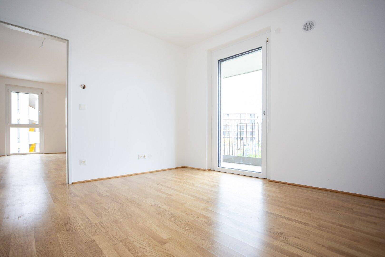 Heller Raum mit Parkettboden und Zugang zu einem Balkon, ideal für ein Schlaf- oder Wohnzimmer.