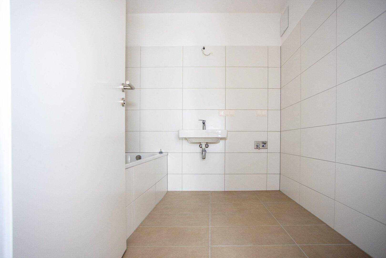 Modernes Badezimmer mit weißen Fliesen, Waschbecken und einer Badewanne, bereit zur Nutzung.