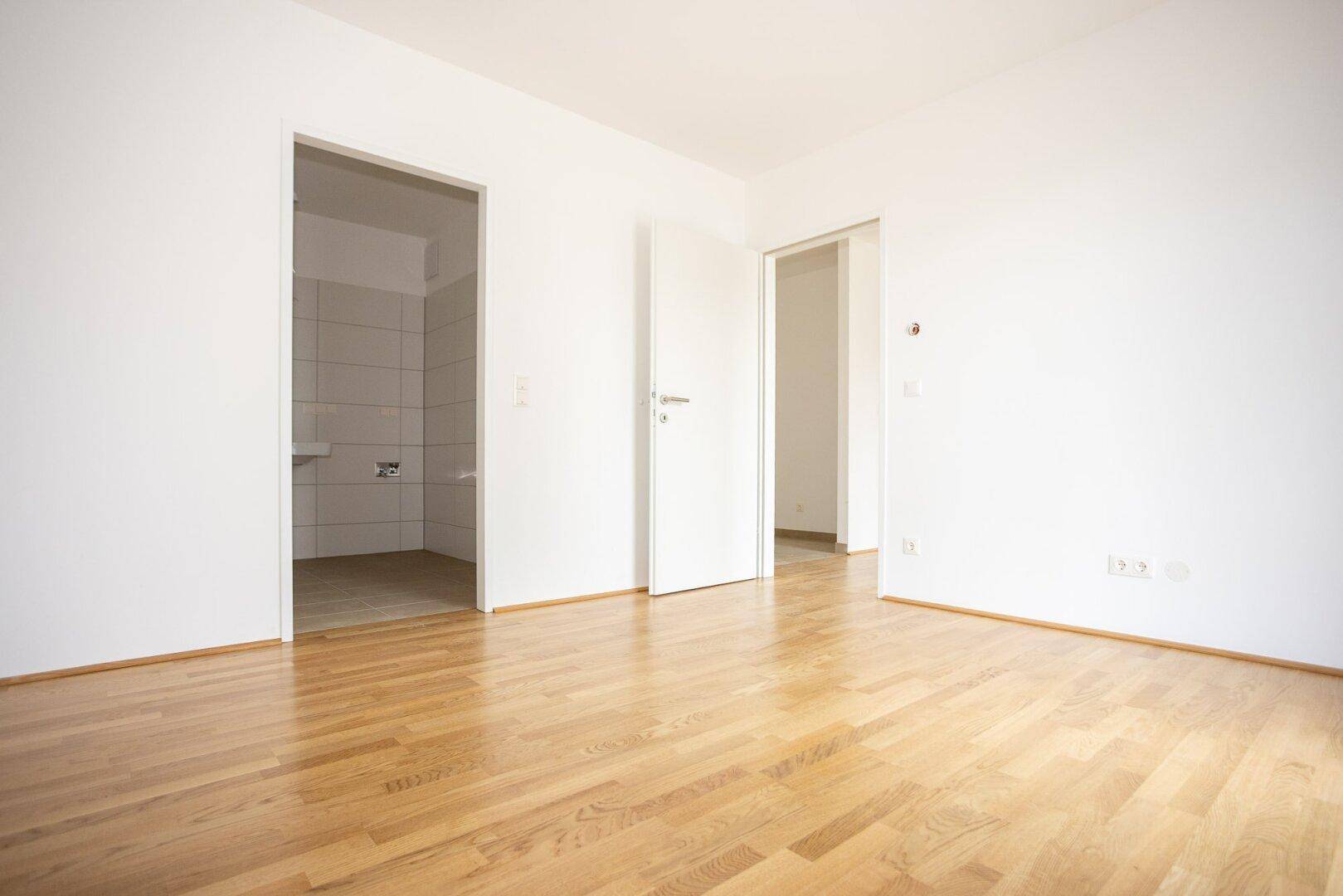Geräumiger Raum mit Parkettboden und offenem Zugang zu einem gefliesten Badezimmer.