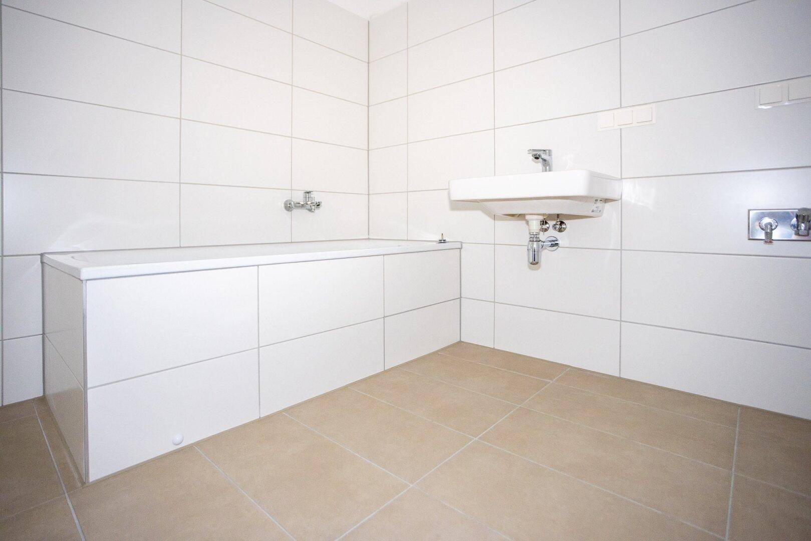 Helles Badezimmer mit weißen Wandfliesen, integrierter Badewanne und modernem Waschbecken.