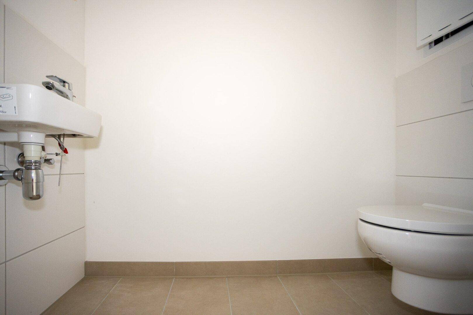 Kleines Gäste-WC mit wandmontierter Toilette und kompaktem Waschbecken, funktional und hell.