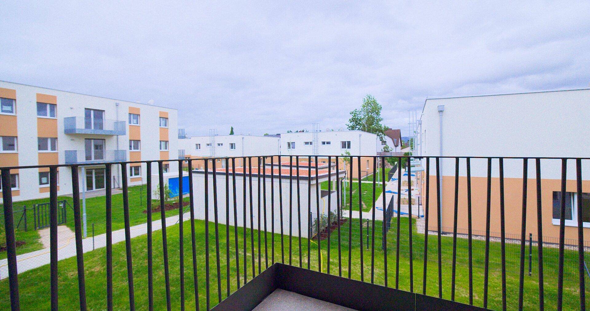 Balkon mit Aussicht auf den Innenhof und weitere Neubauten, umgeben von viel Grün.