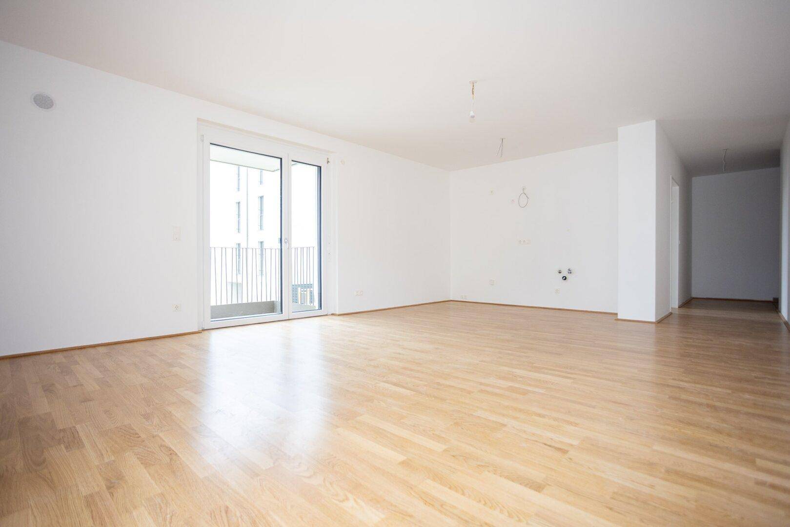 Geräumiger, heller Wohnbereich mit Parkettboden und Zugang zu einem Balkon.