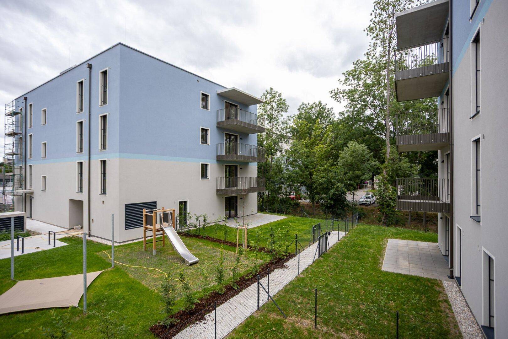 Außenansicht eines modernen Wohngebäudes mit Spielplatz und gepflegter Rasenfläche.