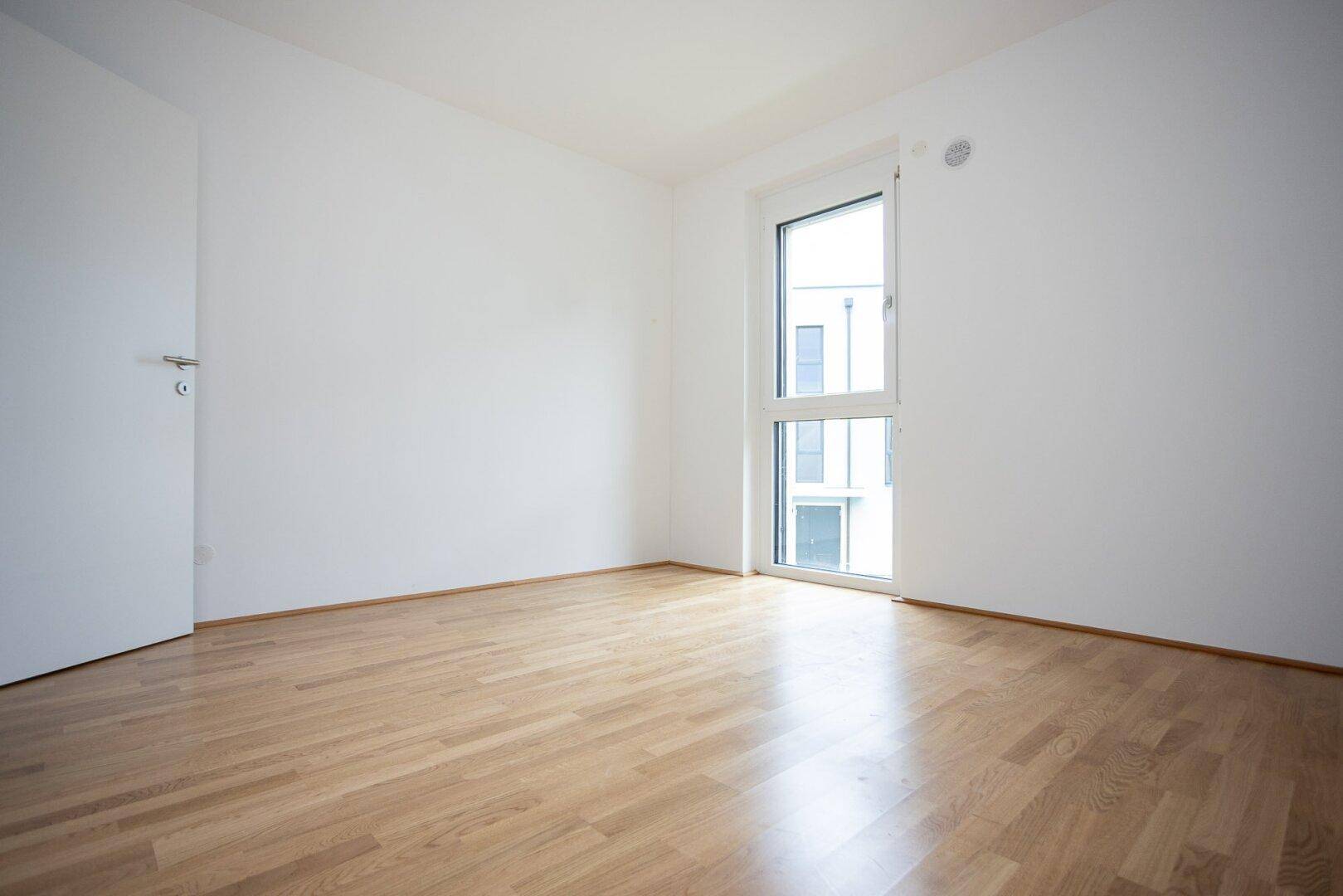 Helles Schlafzimmer mit Parkettboden und weiß gestrichenen Wänden, bereit zur Einrichtung.