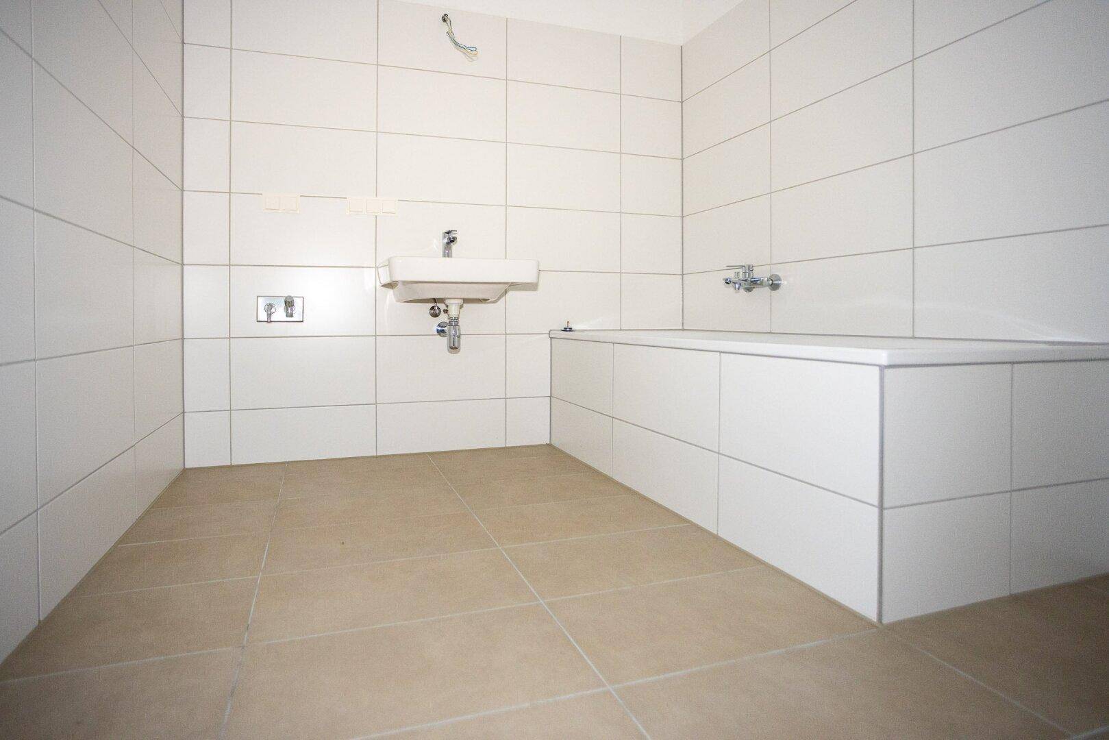 Modernes Badezimmer mit weißen Wandfliesen, beigefarbenem Boden und einer Badewanne.