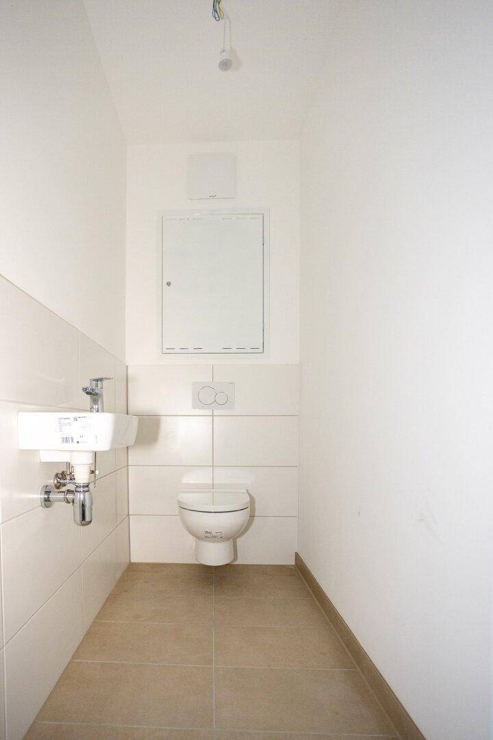 Kleines Gäste-WC mit wandhängender Toilette, Waschbecken und hellen Fliesen.