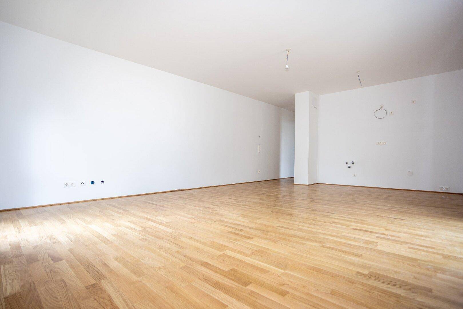 Geräumiges, leeres Zimmer mit hellem Holzboden und weißen Wänden, bereit für die Einrichtung.