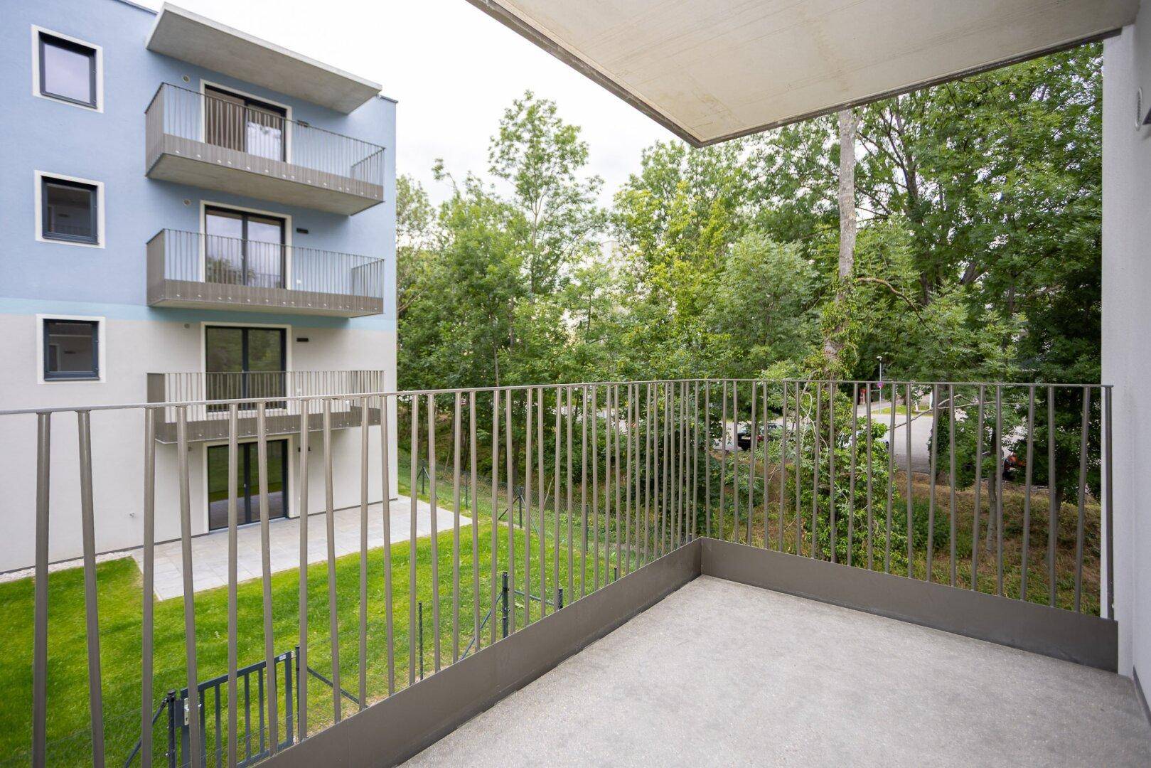 Balkon mit Blick auf eine grüne Rasenfläche und Bäume, umgeben von modernen Gebäuden.