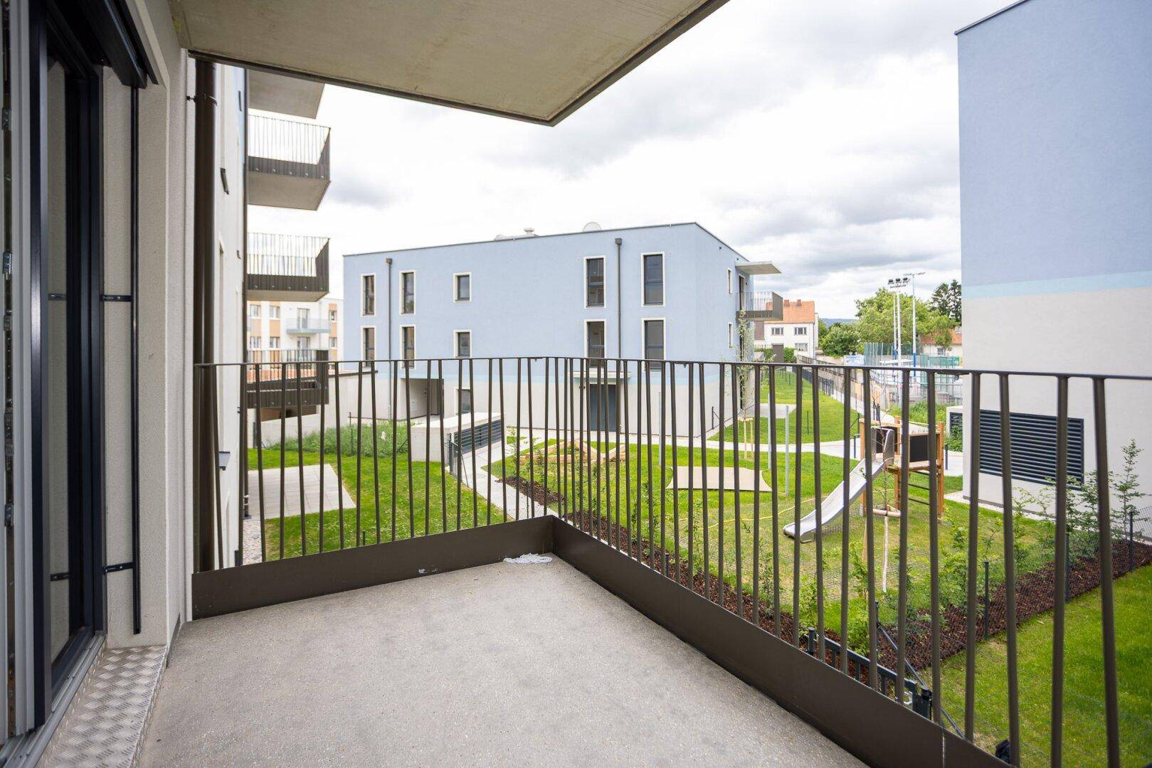 Balkon mit Blick auf den Gemeinschaftsgarten und einen Spielplatz zwischen modernen Gebäuden.