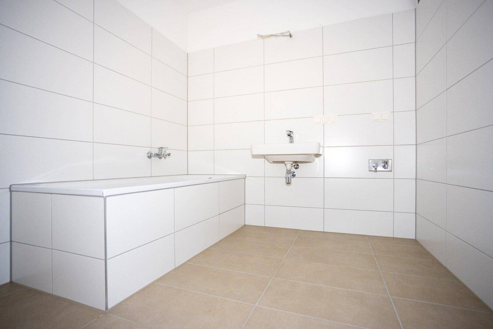 Modernes Badezimmer mit weißen Wandfliesen, beigem Boden und einer eingebauten Badewanne.