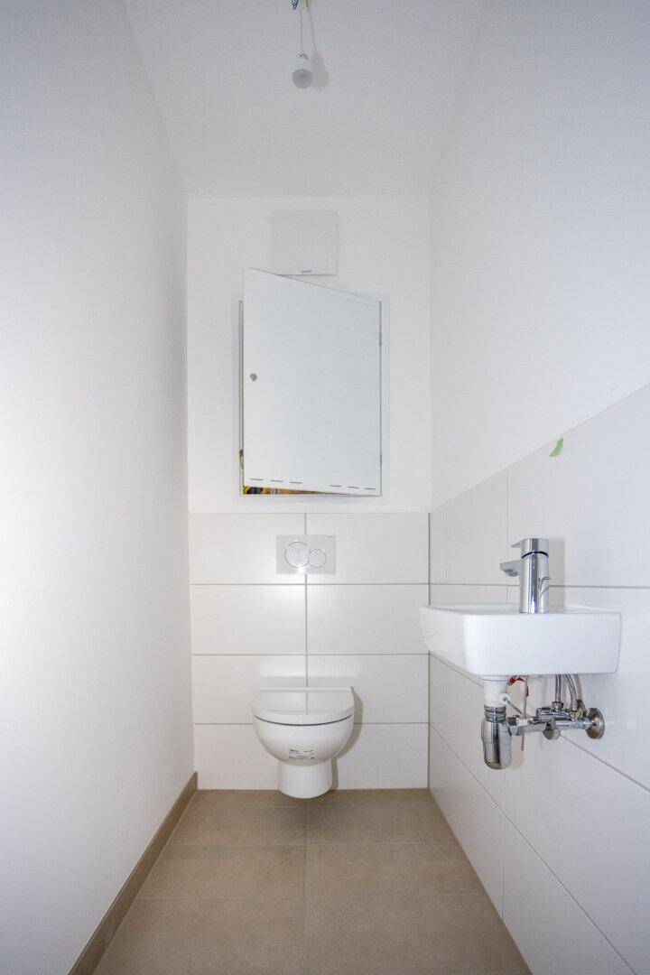 Kleines Gäste-WC mit wandhängender Toilette, Waschbecken und Spiegelschrank.