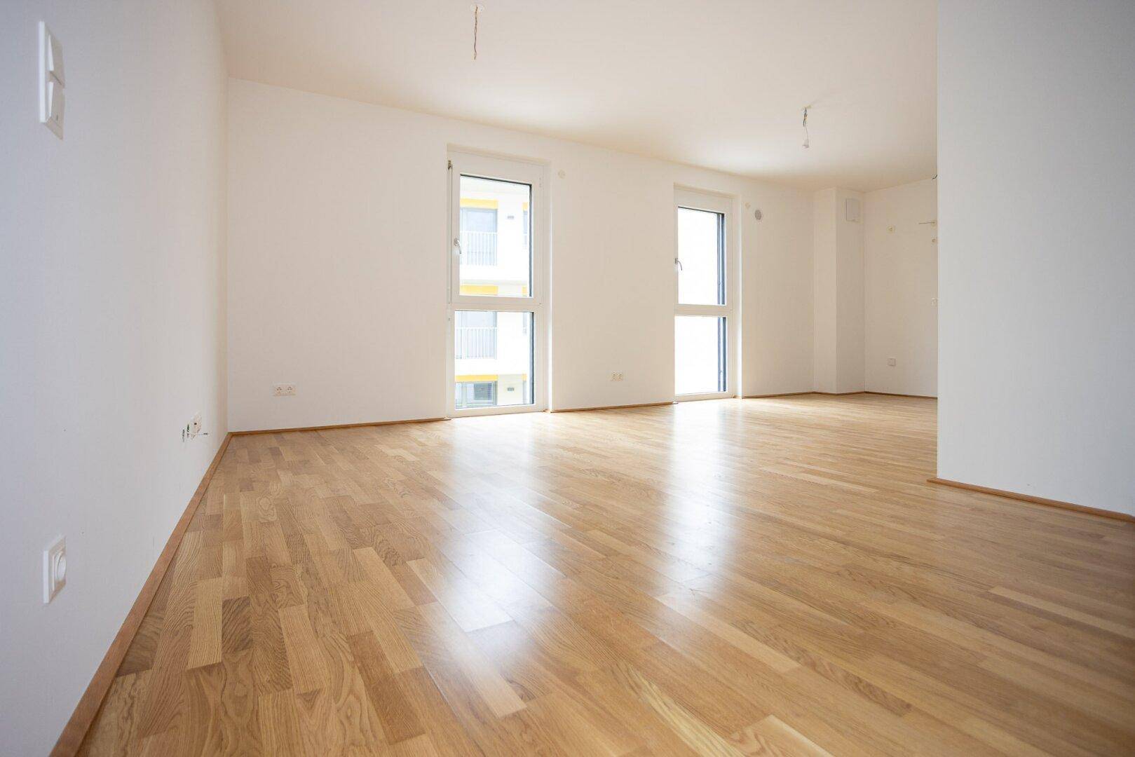 Geräumiges, helles Zimmer mit glänzendem Parkettboden und zwei großen Fenstern.