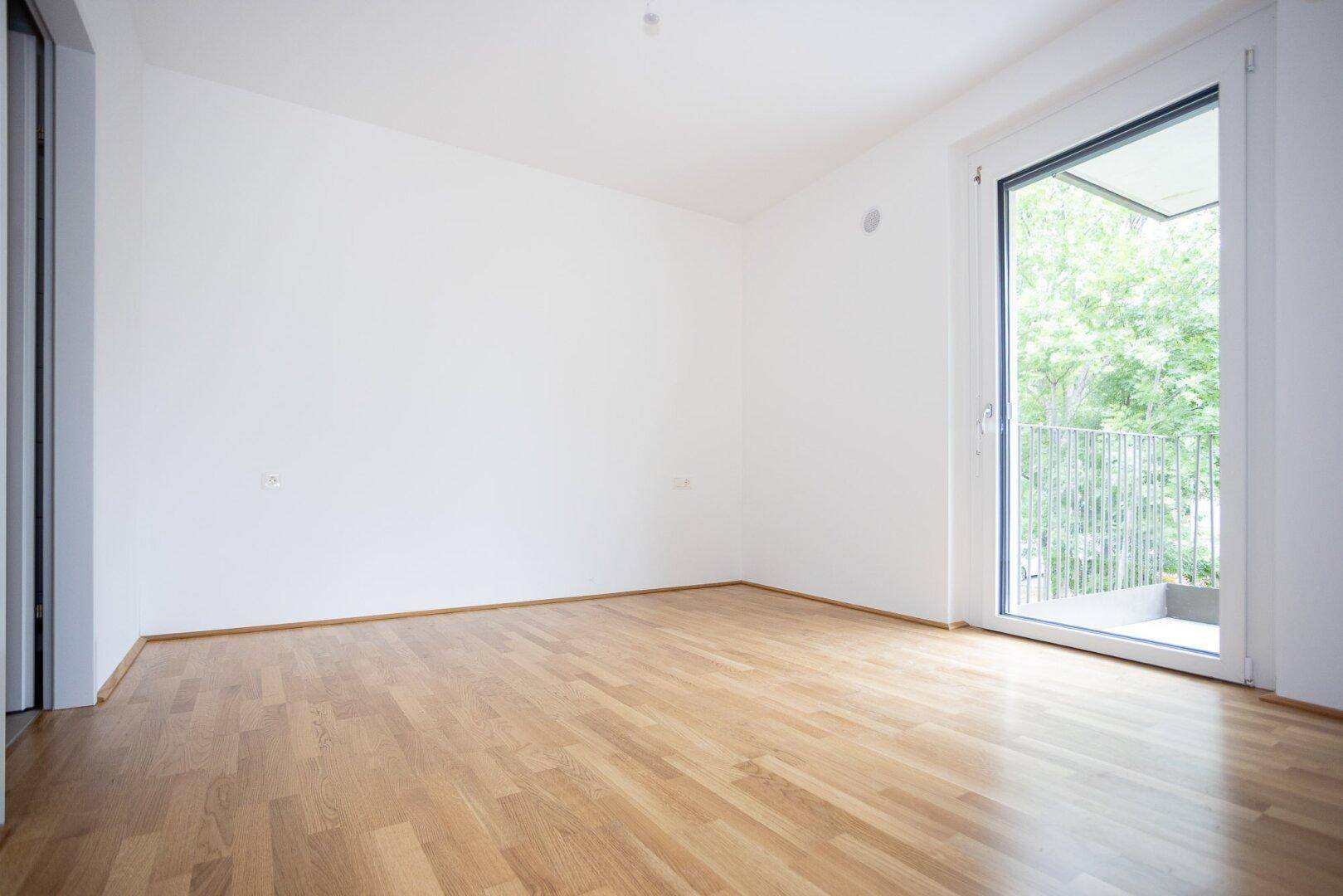 Helles Schlafzimmer mit Parkettboden und direktem Zugang zu einem Balkon mit Grünblick.