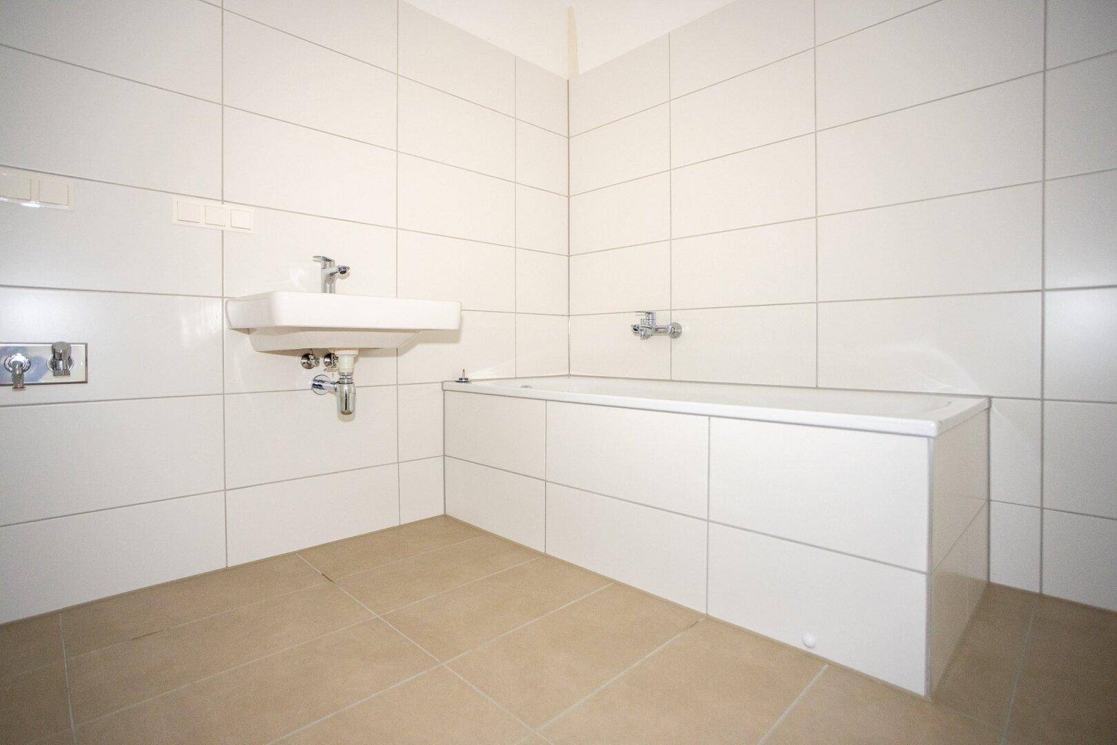 Modernes Badezimmer mit weißen Fliesen, einem Waschbecken und einer eingebauten Badewanne.