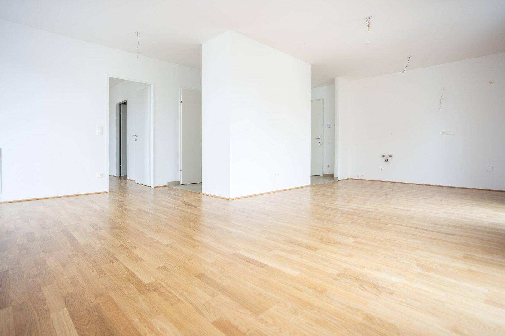 Geräumiges, leeres Zimmer mit hellem Parkettboden und Zugang zu weiteren Räumen.