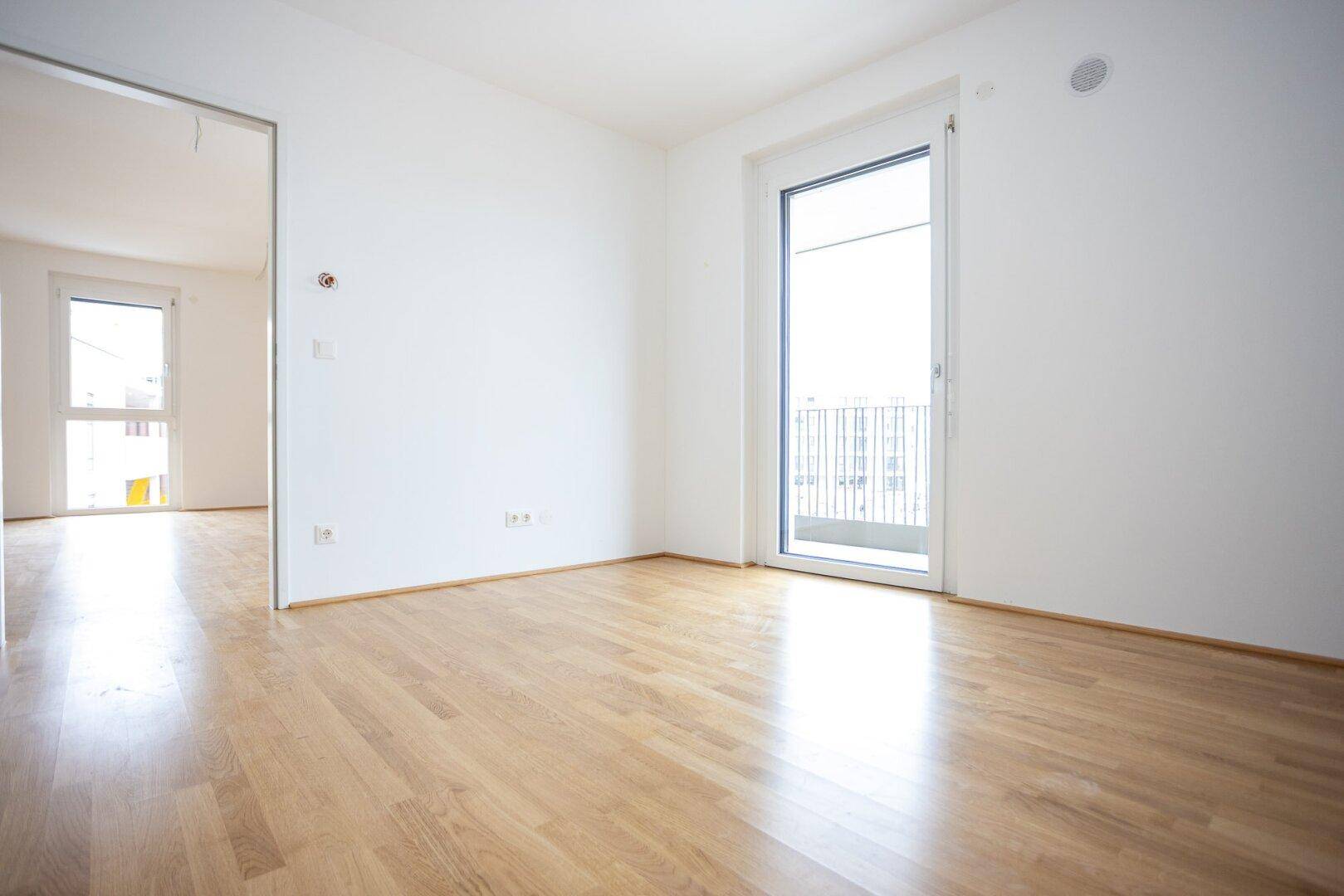 Helles Zimmer mit Parkettboden und Zugang zu einem französischen Balkon.