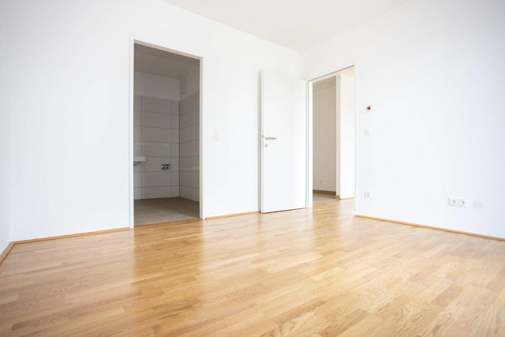 Leeres Zimmer mit Parkettboden und offenem Zugang zu einem gefliesten Bereich.