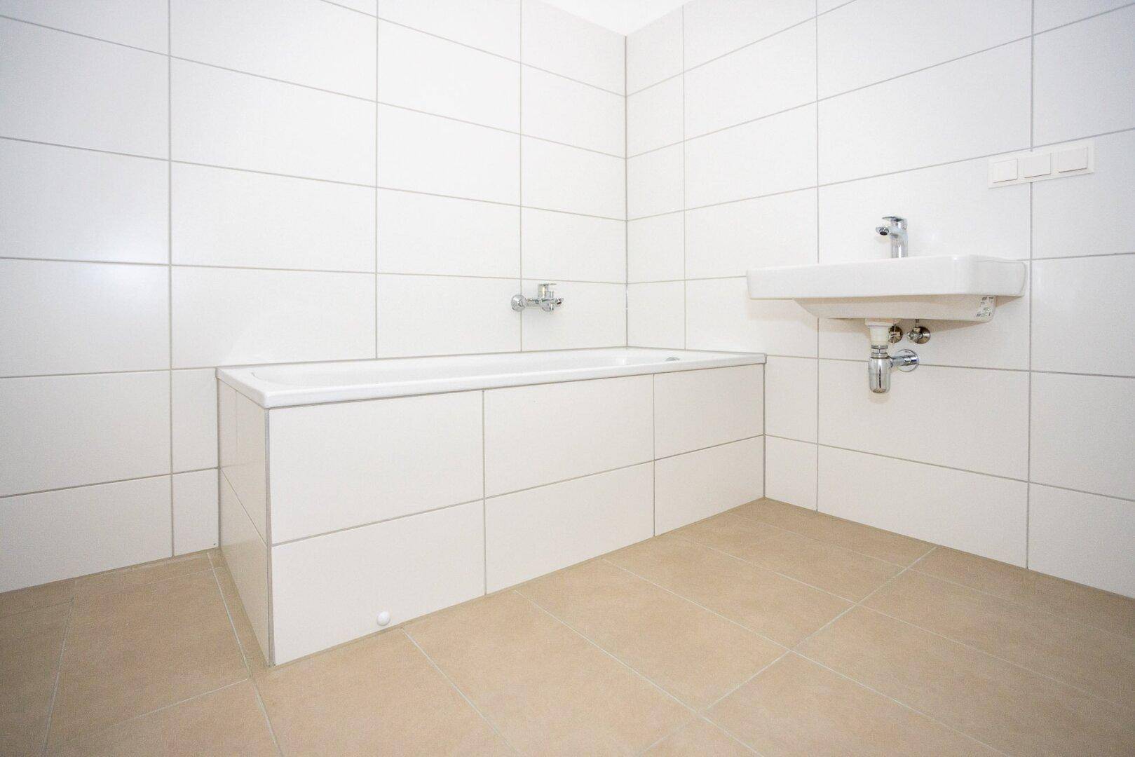 Modernes Badezimmer mit weißen Fliesen, integrierter Badewanne und Waschbecken.