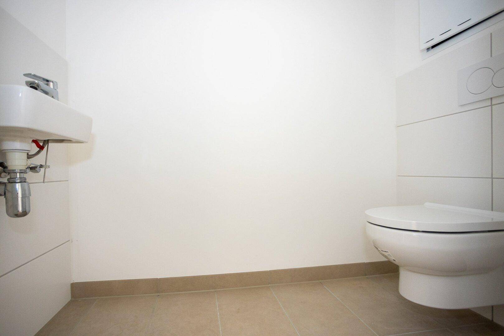 Separates WC mit wandhängender Toilette und kleinem Handwaschbecken.