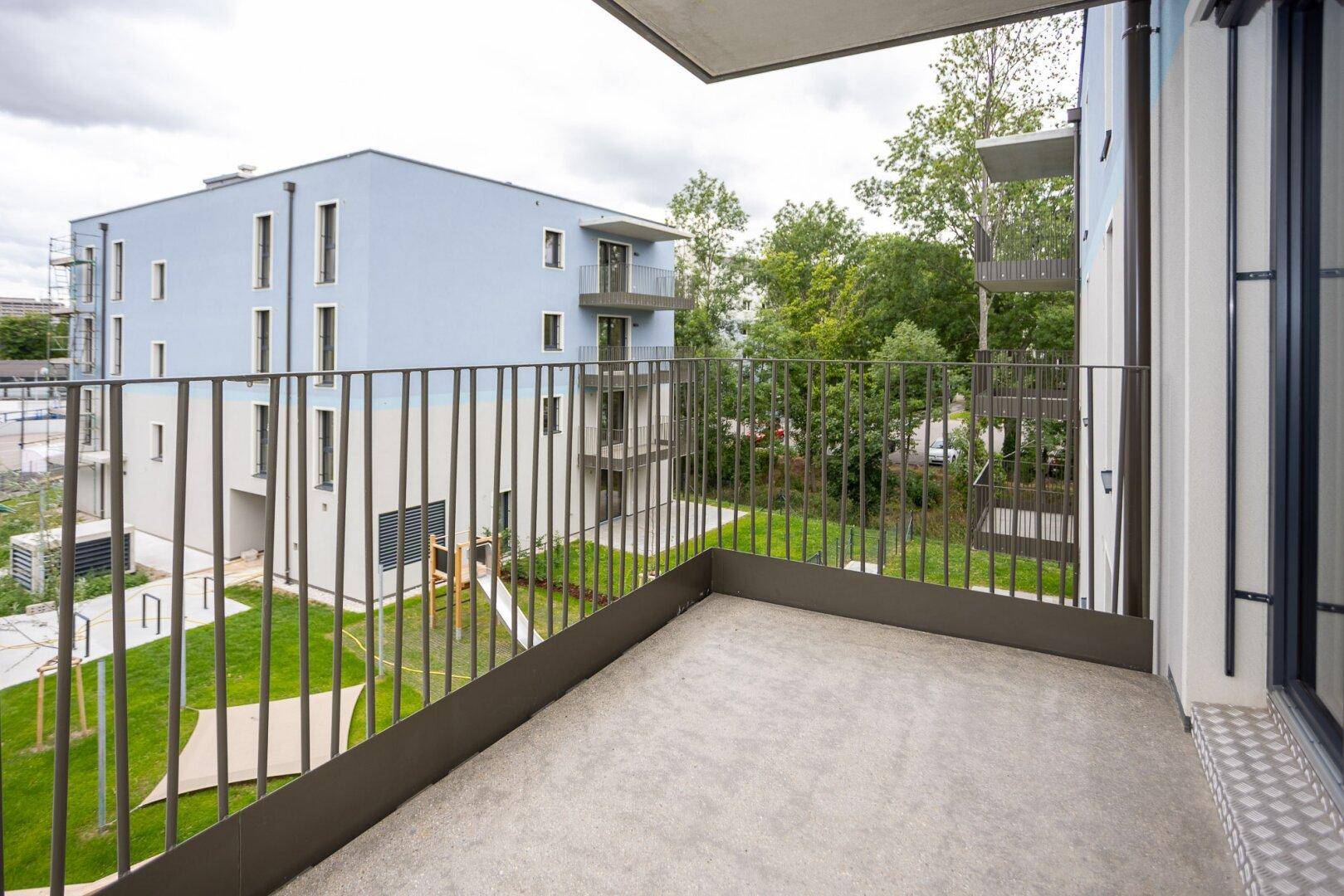 Balkon mit modernem Metallgeländer und Blick auf die umliegenden Neubauten und Grünflächen.