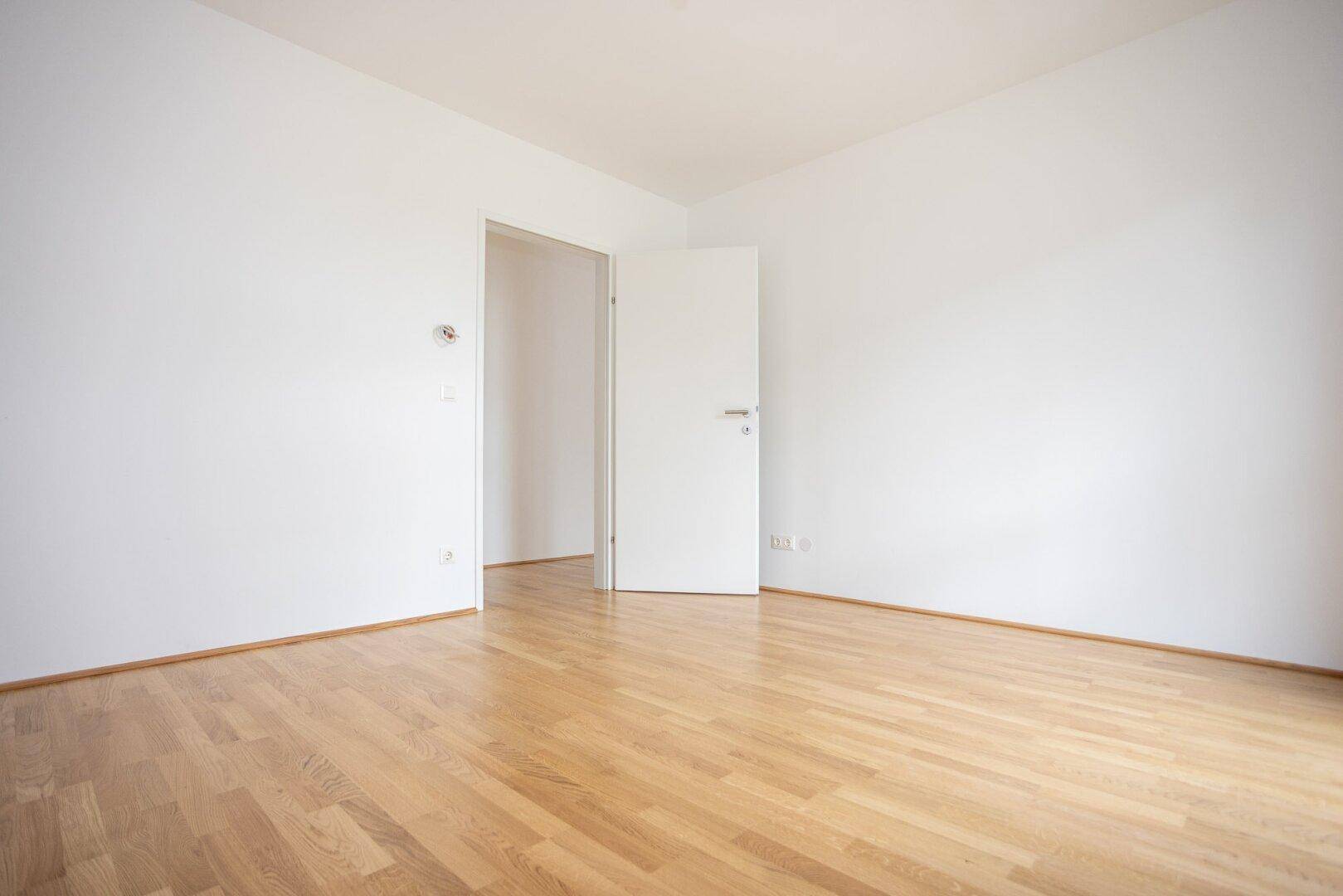 Leeres Zimmer mit Parkettboden und weiß gestrichenen Wänden, bereit zur individuellen Gestaltung.