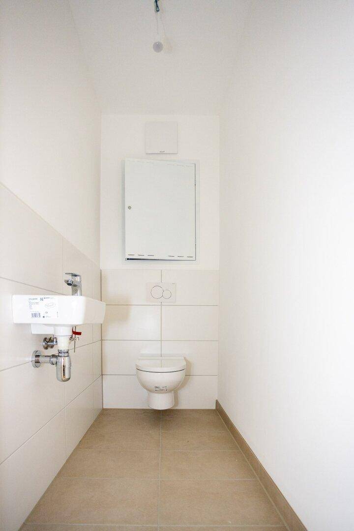 Separates Gäste-WC mit wandhängender Toilette und kleinem Waschbecken, modern gefliest.