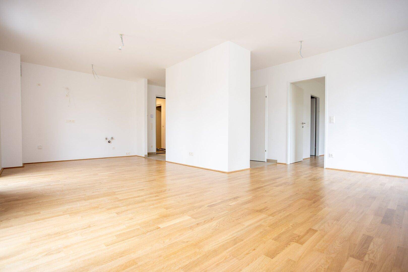 Geräumiges, leeres Zimmer mit hellem Laminatboden und weißen Wänden, ideal für individuelle Gestaltung.