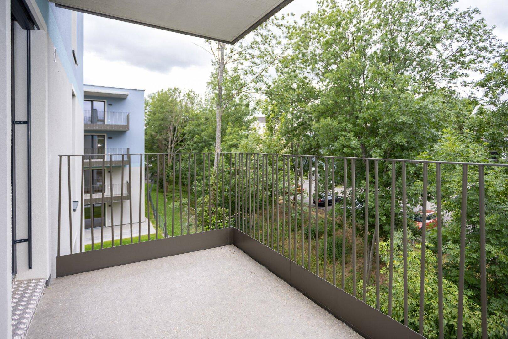 Moderner Balkon mit Blick auf die grüne Umgebung und angrenzende Neubauten.