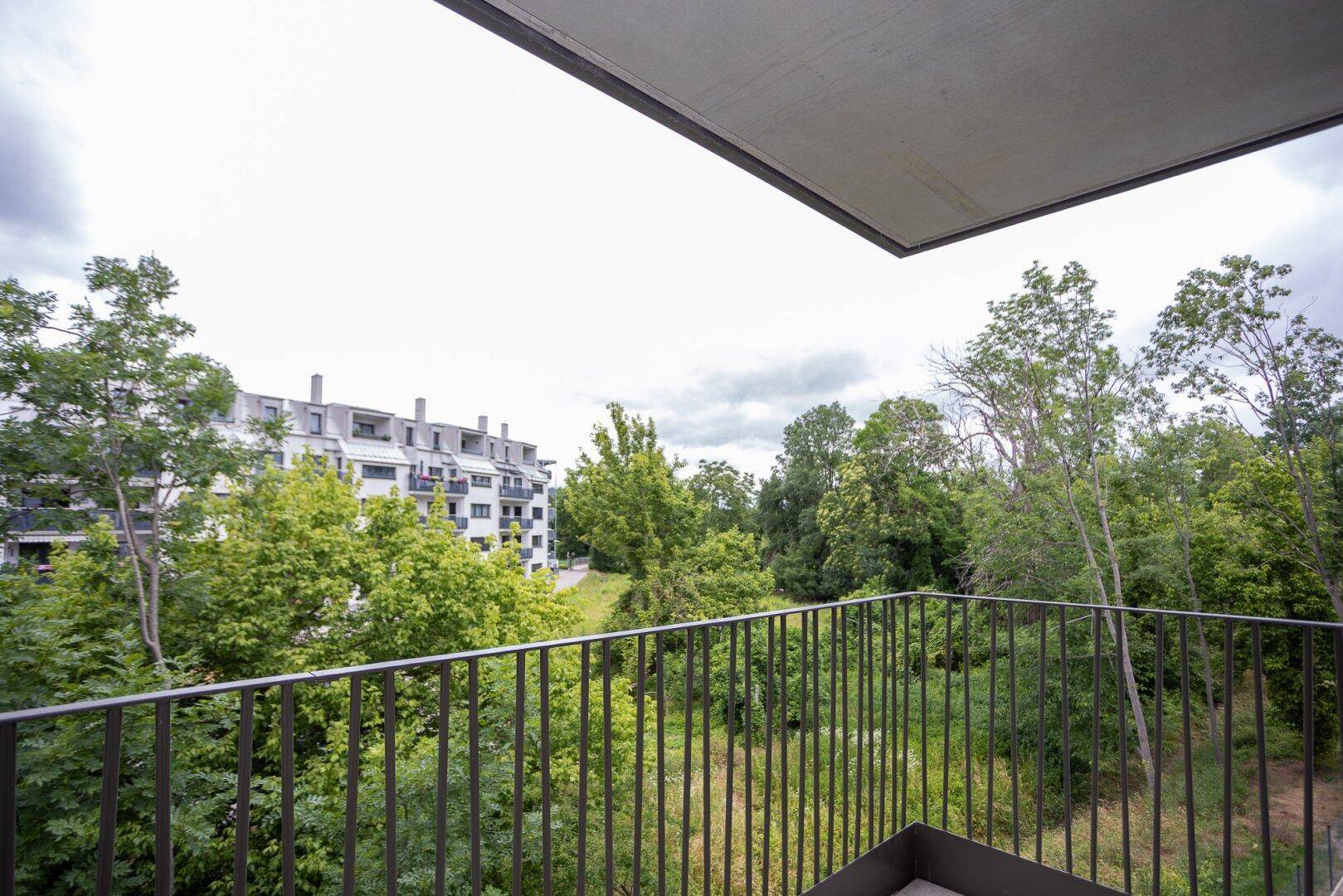 Balkon mit Metallgeländer und Blick ins Grüne sowie auf umliegende Gebäude.