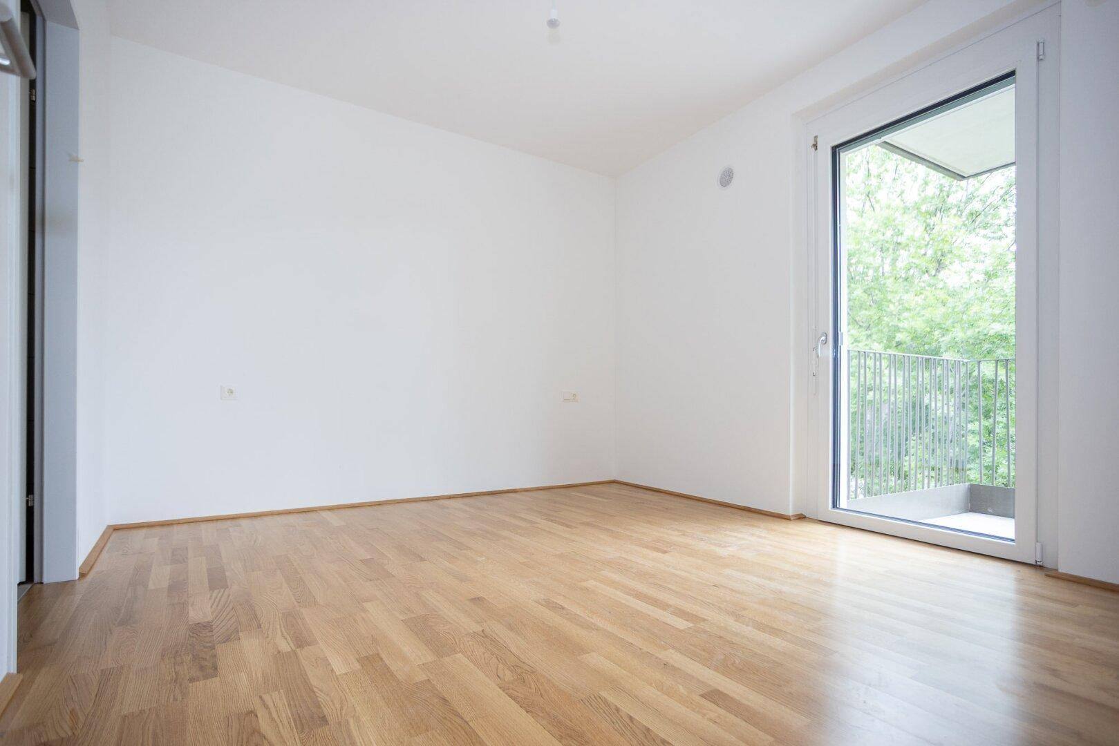 Helles Schlafzimmer mit Balkonzugang und Laminatboden, bietet einen ruhigen Rückzugsort.