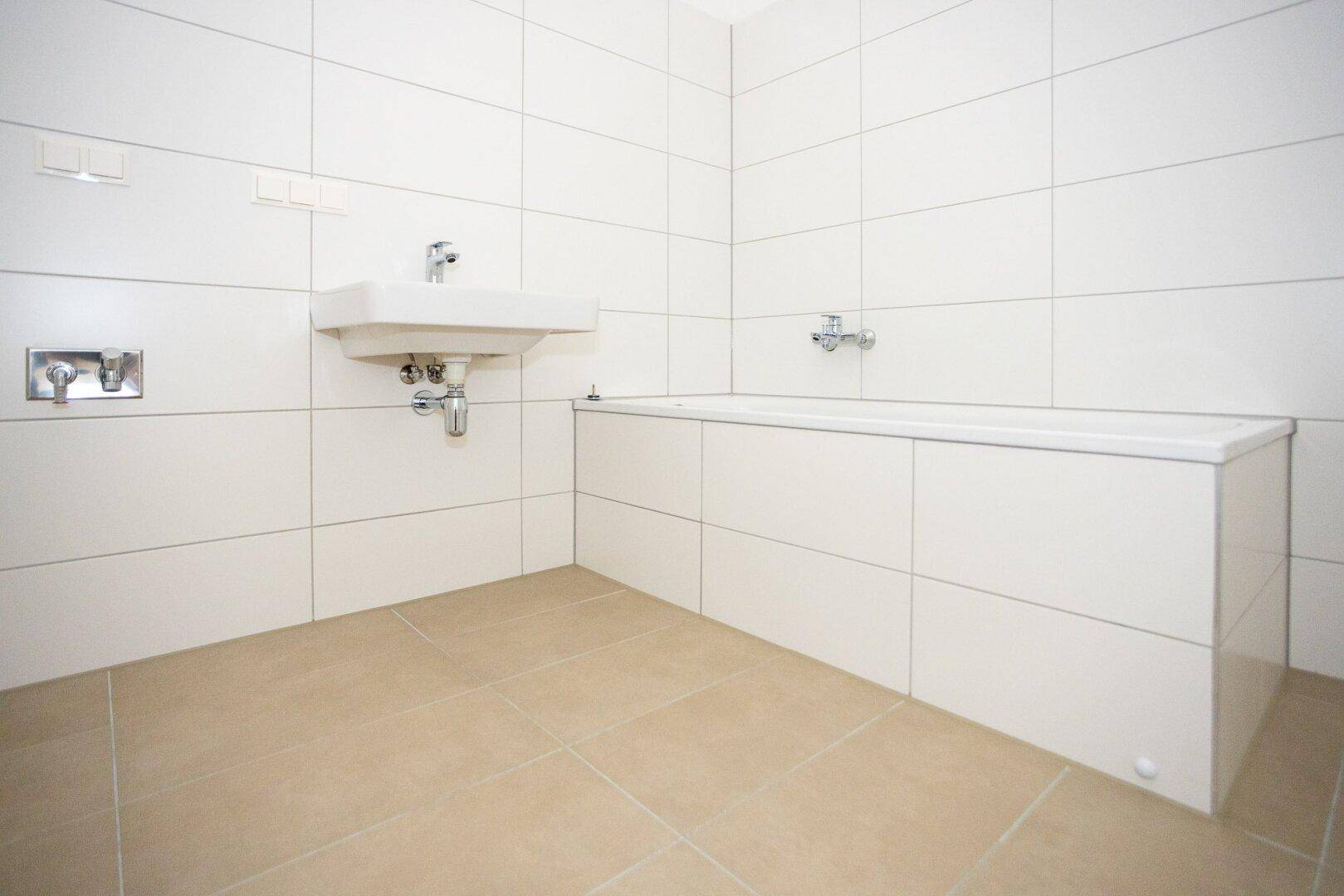 Modernes Badezimmer mit weißen Fliesen, Badewanne und Waschbecken, in neuwertigem Zustand.