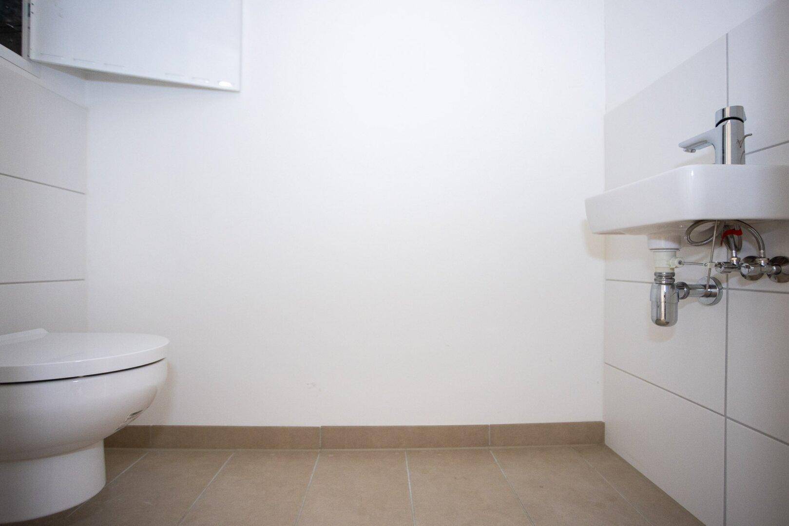Kleines Gäste-WC mit Wand-WC und Waschbecken, ausgestattet mit hellen Fliesen.