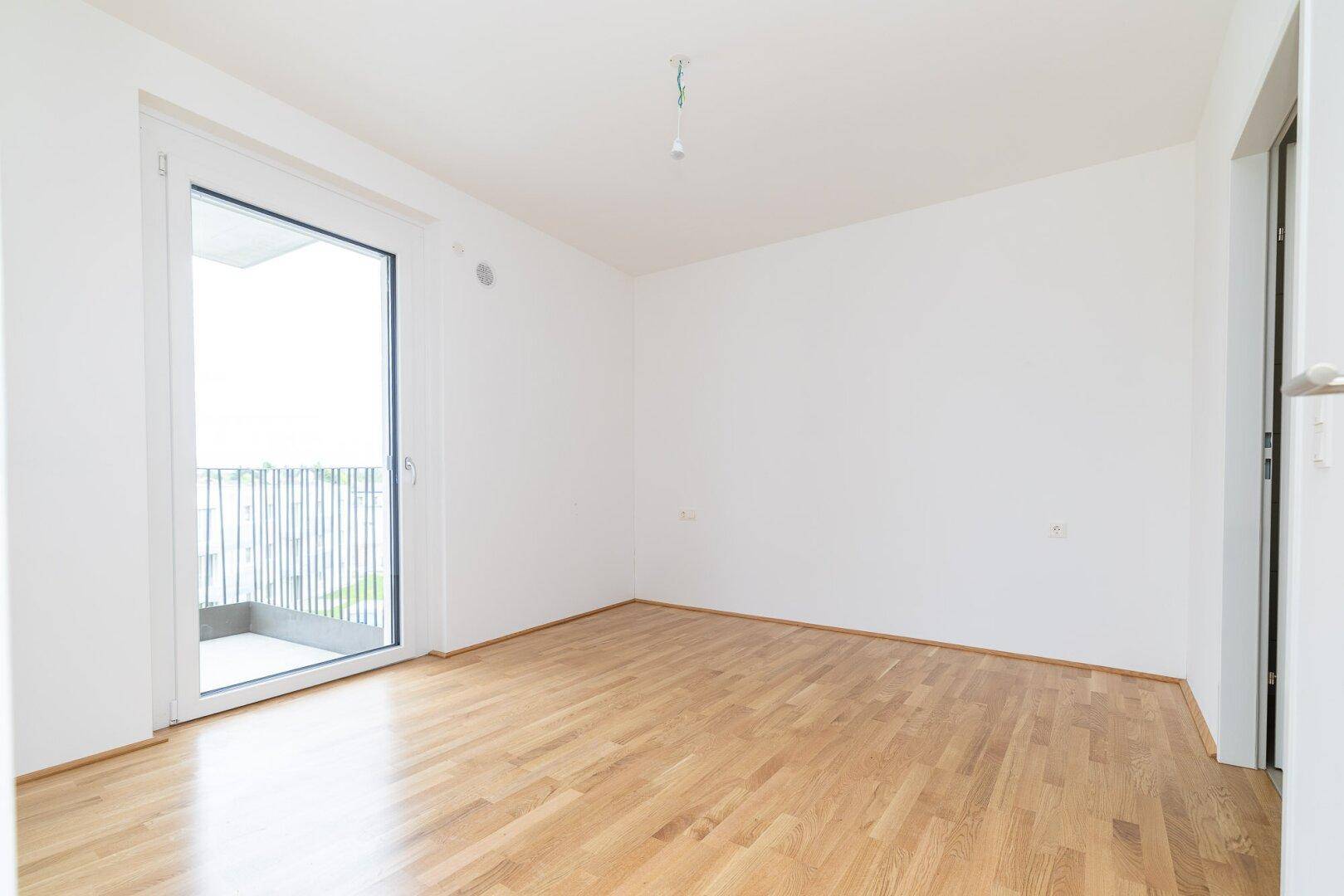 Helles Schlafzimmer mit Parkettboden und direktem Zugang zu einem Außenbalkon.
