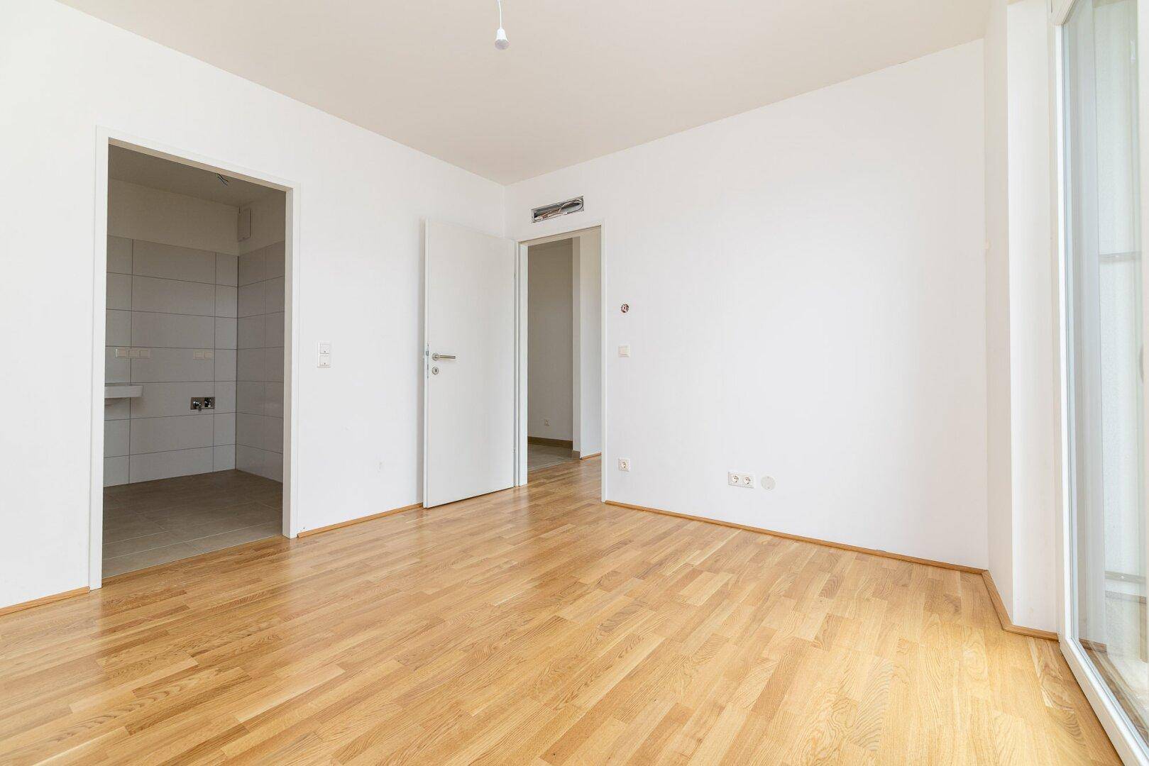 Geräumiges Zimmer mit Parkettboden und Zugang zu einem angrenzenden Badezimmer.