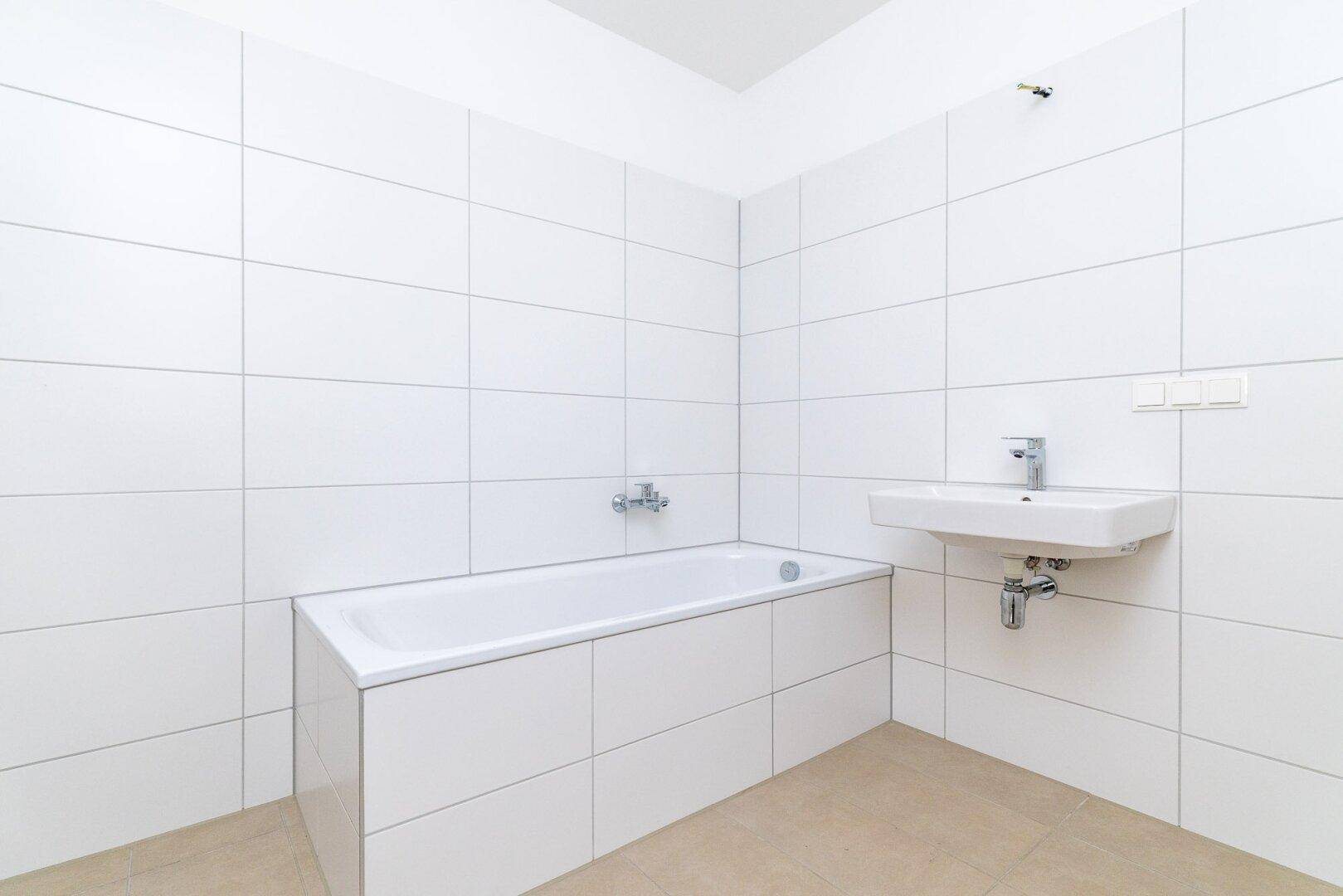 Modernes Badezimmer mit weißen Fliesen, Badewanne und einem einzelnen Waschbecken.