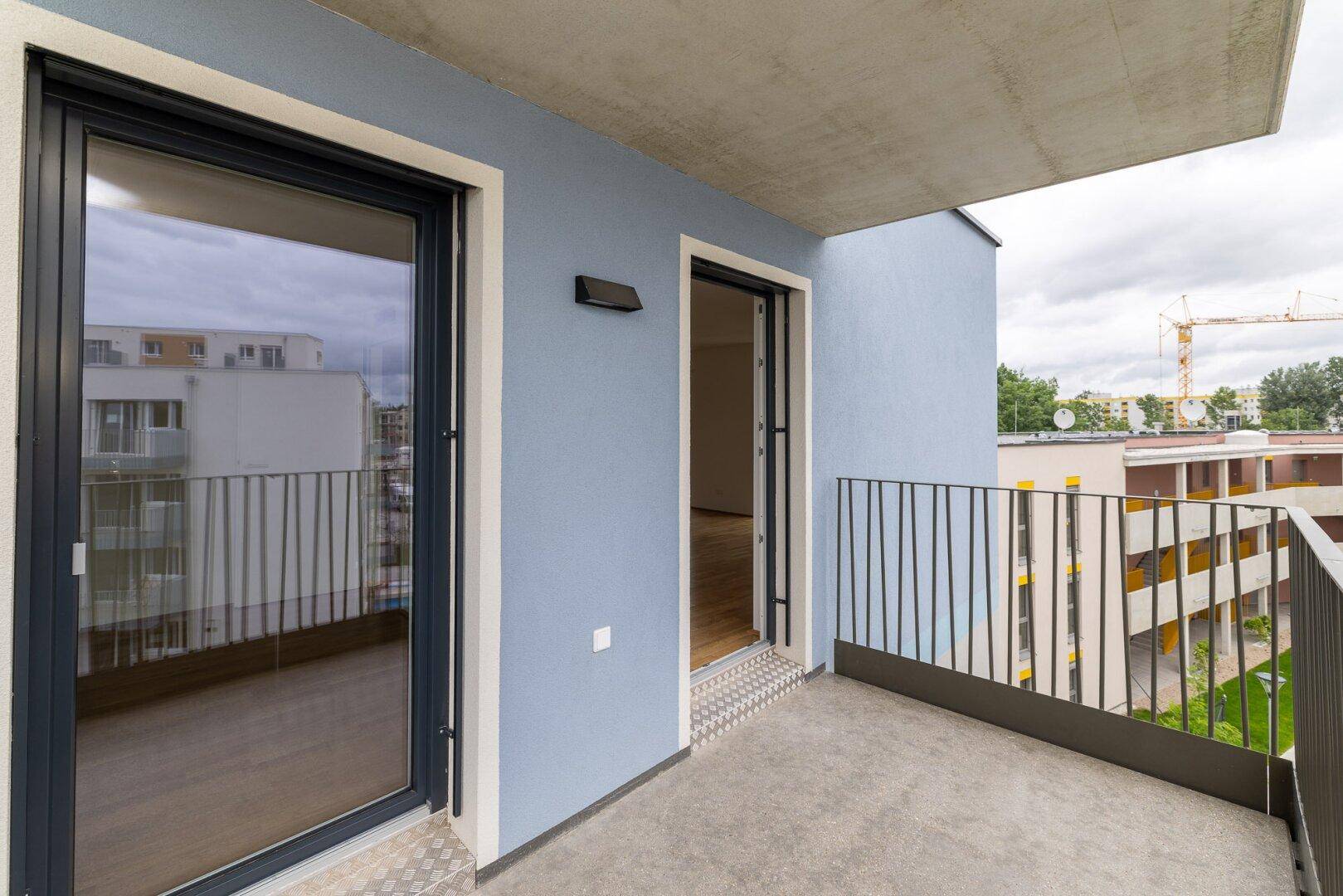 Balkon mit Zugangstür und Blick auf die Nachbarschaft sowie einen Baukran in der Ferne.