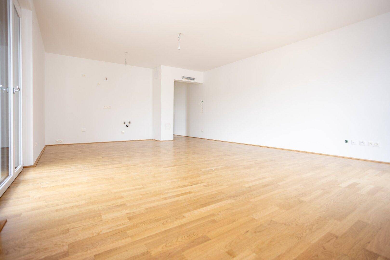 Großes, leeres Zimmer mit Parkettboden und Anschlüssen, ideal für offenes Wohnen.