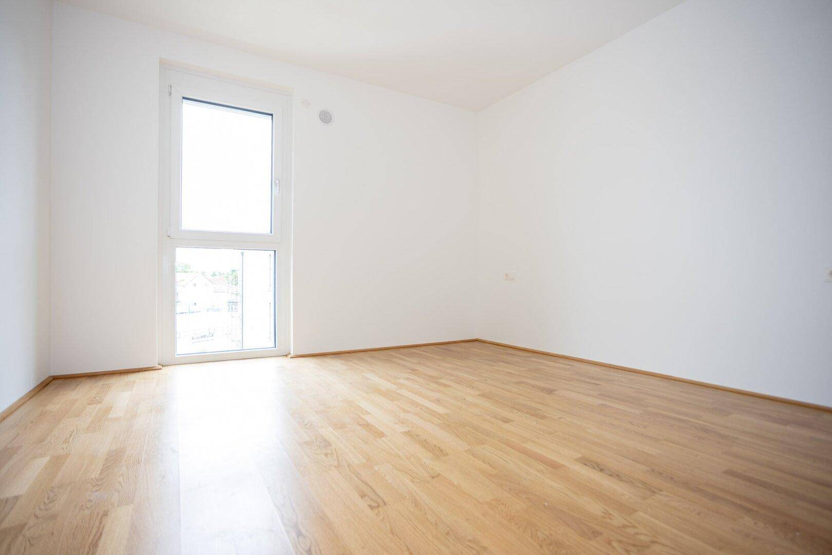 Helles Schlafzimmer mit Parkettboden und großem Fenster, ideal für viel Tageslicht.